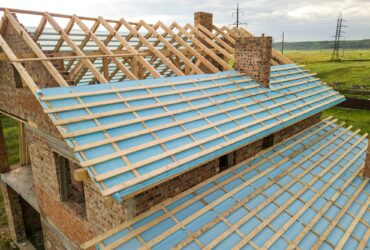 Aerial view of a brick house with wooden roof frame under construction.