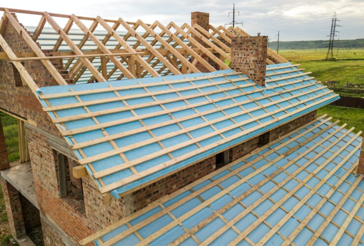 Aerial view of a brick house with wooden roof frame under construction.