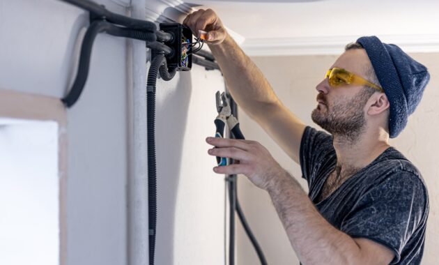 An electrician is mounting electric sockets on the white wall indoors.