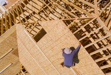 Carpenter with nailing plywood on roof of the house