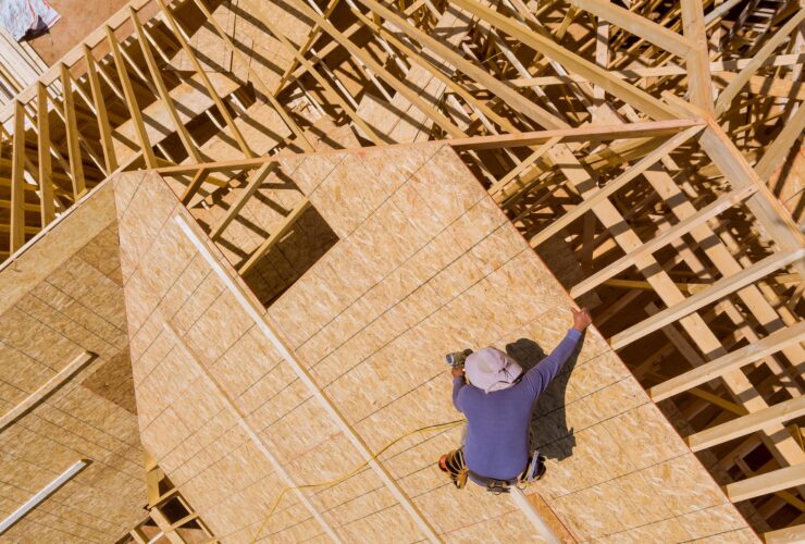 Carpenter with nailing plywood on roof of the house