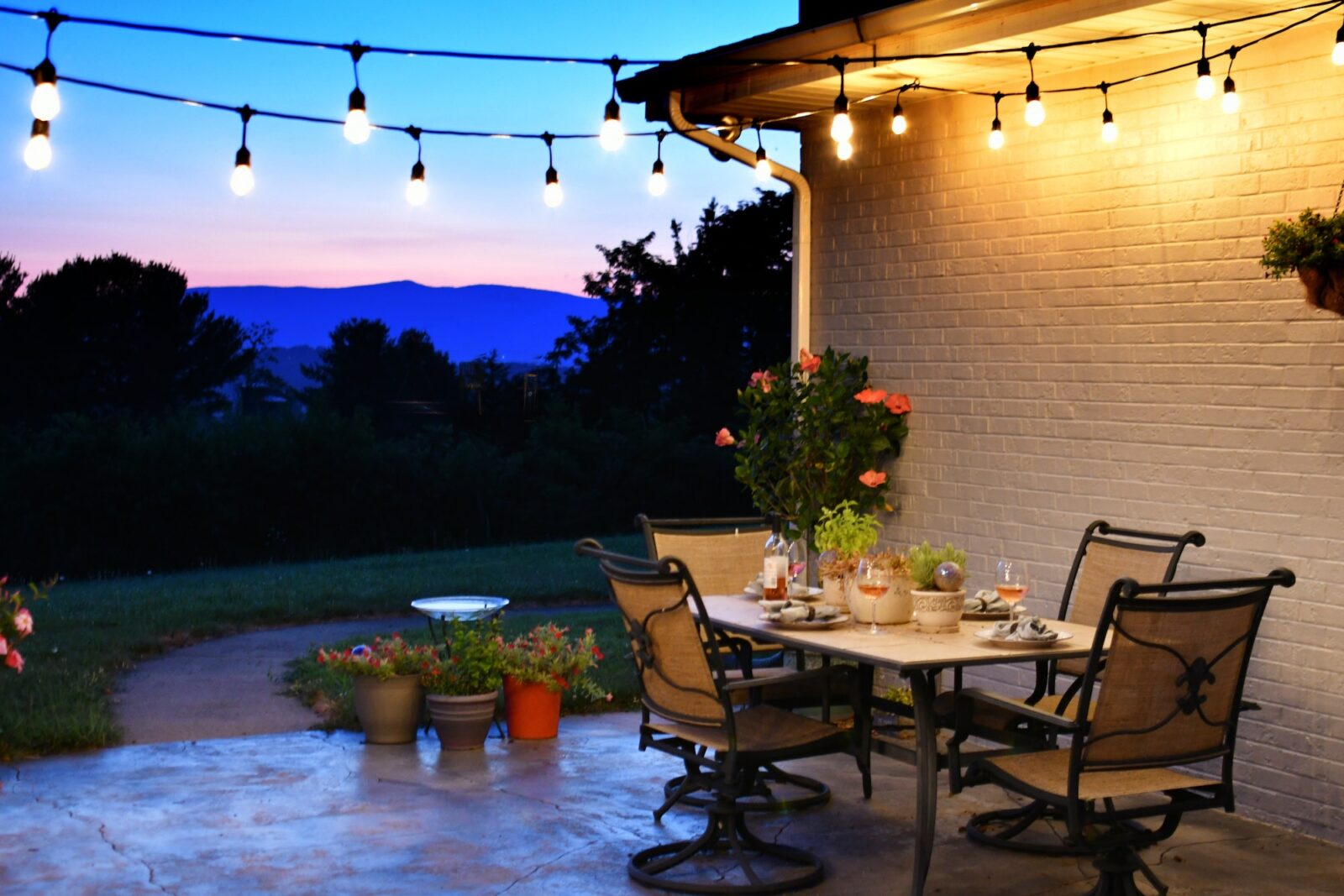 Outdoor living space with dining table set for dinner with wine, lights and a view of the mountains