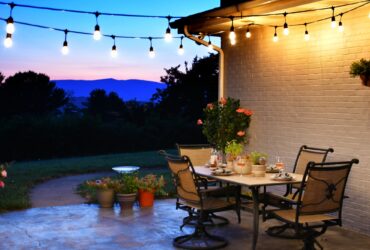 Outdoor living space with dining table set for dinner with wine, lights and a view of the mountains