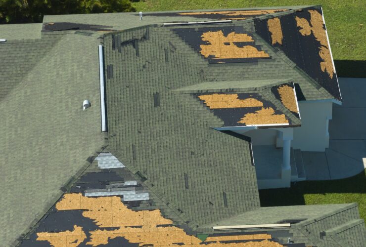 Wind damaged house roof with missing asphalt shingles after hurricane Ian in Florida.