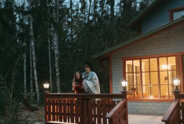 A couple wrapped in a blanket enjoys a winter evening on a forest cabin balcony.