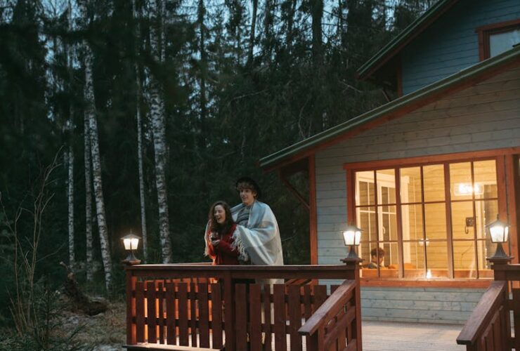 A couple wrapped in a blanket enjoys a winter evening on a forest cabin balcony.