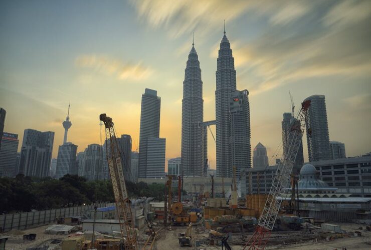 Dramatic view of the Petronas Towers towering over a busy construction site in Kuala Lumpur at sunset.