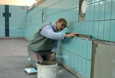 Tiler expertly aligns ceramic tiles on a swimming pool wall. Indoor construction setting in Wrocław.