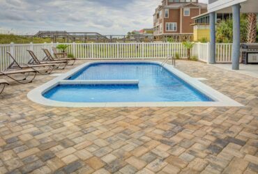 Relaxing poolside patio with sun loungers and villas, perfect for a summer retreat.