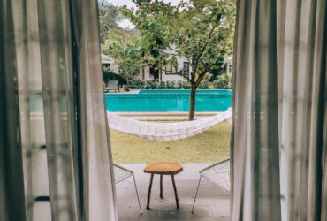Charming poolside view through curtains with hammock and seating, ideal for a summer vacation.