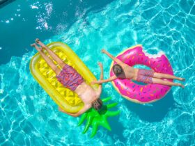 Two boys sunbathing on colorful pool floats, enjoying a sunny day in a clear blue swimming pool.