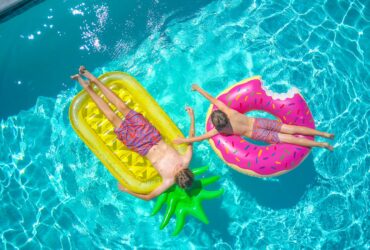 Two boys sunbathing on colorful pool floats, enjoying a sunny day in a clear blue swimming pool.