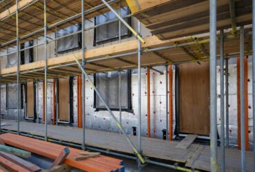 Scaffolding at a residential building under construction with windows and insulation sheets visible.