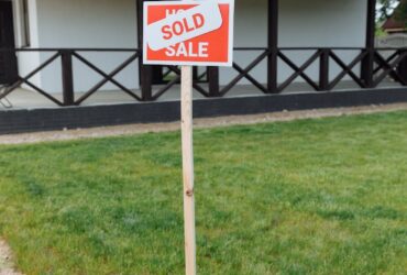A modern house with a sold sign on a grassy lawn, indicating property purchase.