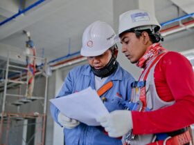Two engineers in safety helmets reviewing construction plans at a worksite.