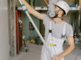 Two construction workers in safety gear are interior renovating, using a paint roller.