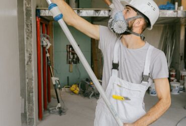 Two construction workers in safety gear are interior renovating, using a paint roller.