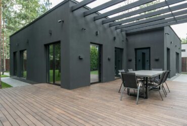 Contemporary black house with spacious wooden terrace and outdoor seating area.