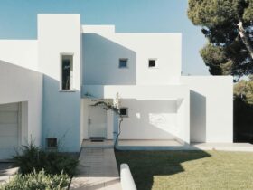 A minimalist modern white house exterior with clean lines and geometric shapes, set against a clear blue sky.