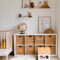 Comfortable bed with toys globe and paintings placed on wooden cabinet with wicker boxes and soft white rug with toy house on floor