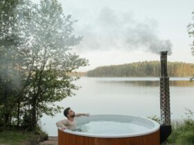 Man enjoying a serene soak in an outdoor hot tub by a peaceful lake surrounded by nature.