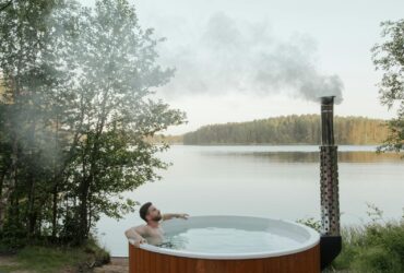 Man enjoying a serene soak in an outdoor hot tub by a peaceful lake surrounded by nature.