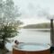 Man enjoying a serene soak in an outdoor hot tub by a peaceful lake surrounded by nature.