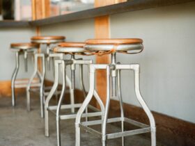 Industrial bar stools with wooden seats lined up in a rustic indoor setting.