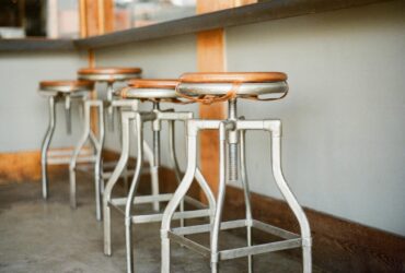 Industrial bar stools with wooden seats lined up in a rustic indoor setting.
