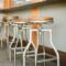 Industrial bar stools with wooden seats lined up in a rustic indoor setting.