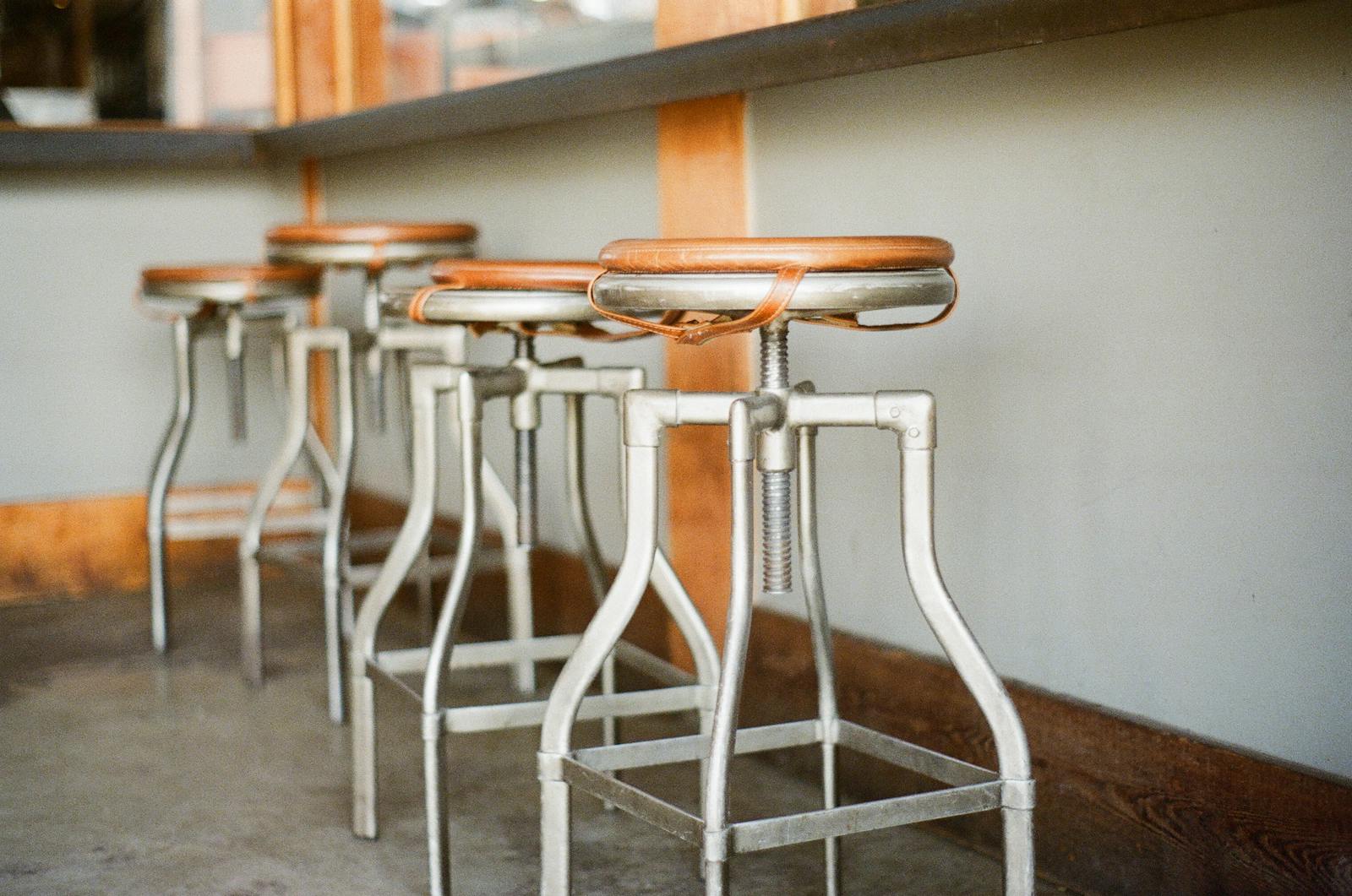 Industrial bar stools with wooden seats lined up in a rustic indoor setting.