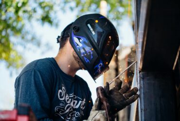 A skilled welder working outside, producing sparks. Shows focus and safety.