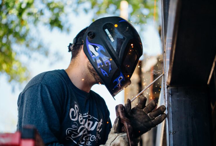 A skilled welder working outside, producing sparks. Shows focus and safety.