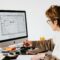 Side view of anonymous female employee in casual clothes and eyeglasses writing out information from computer while working at table in modern light office