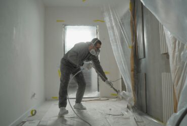 A worker in protective gear painting walls during an indoor renovation project.
