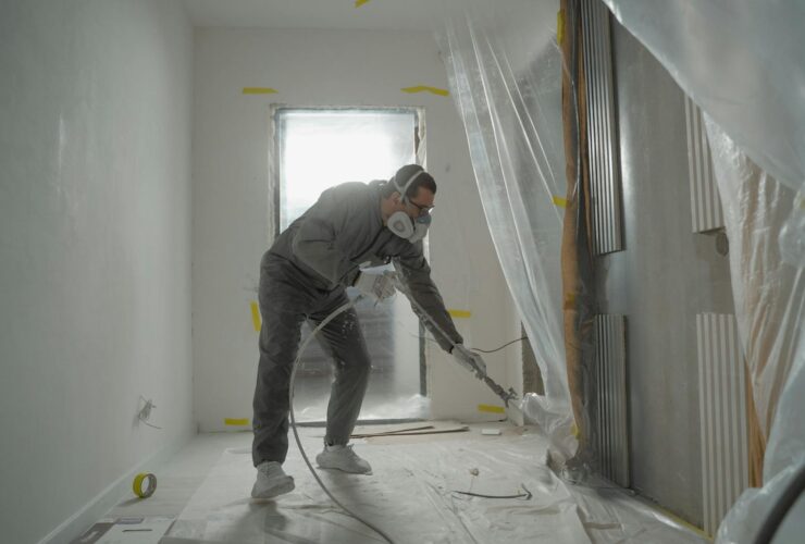 A worker in protective gear painting walls during an indoor renovation project.