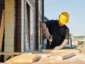A construction worker using a power drill on a building site, outdoors during the day.