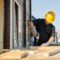 A construction worker using a power drill on a building site, outdoors during the day.