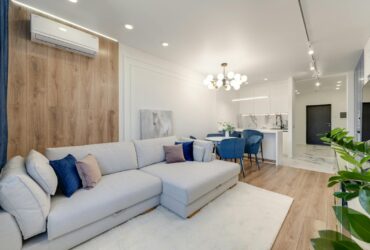 Contemporary living room with stylish furniture, elegant chandelier, and open kitchenette.