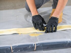 Technician wearing black gloves applying resin to a fiberglass pipe patch during a trenchless CIPP point repair installation.