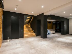 Modern interior with wooden staircase, black walls, and ample space, showcasing minimalistic design.