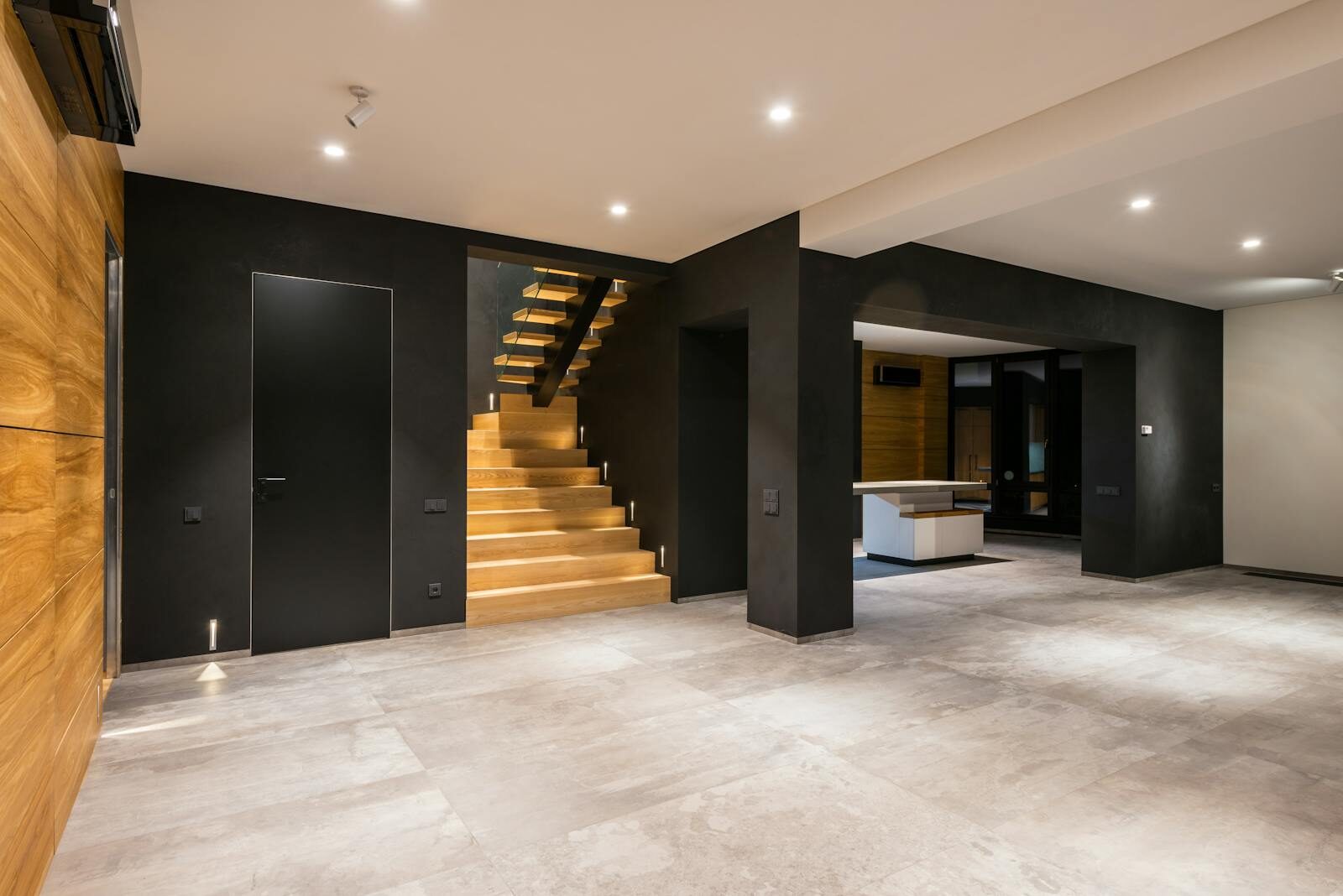 Modern interior with wooden staircase, black walls, and ample space, showcasing minimalistic design.