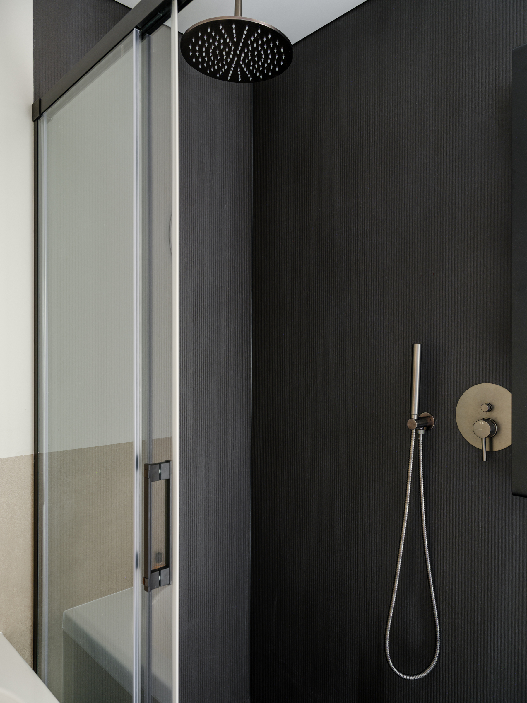 shower area with dark ribbed tiles and brass rain showerhead