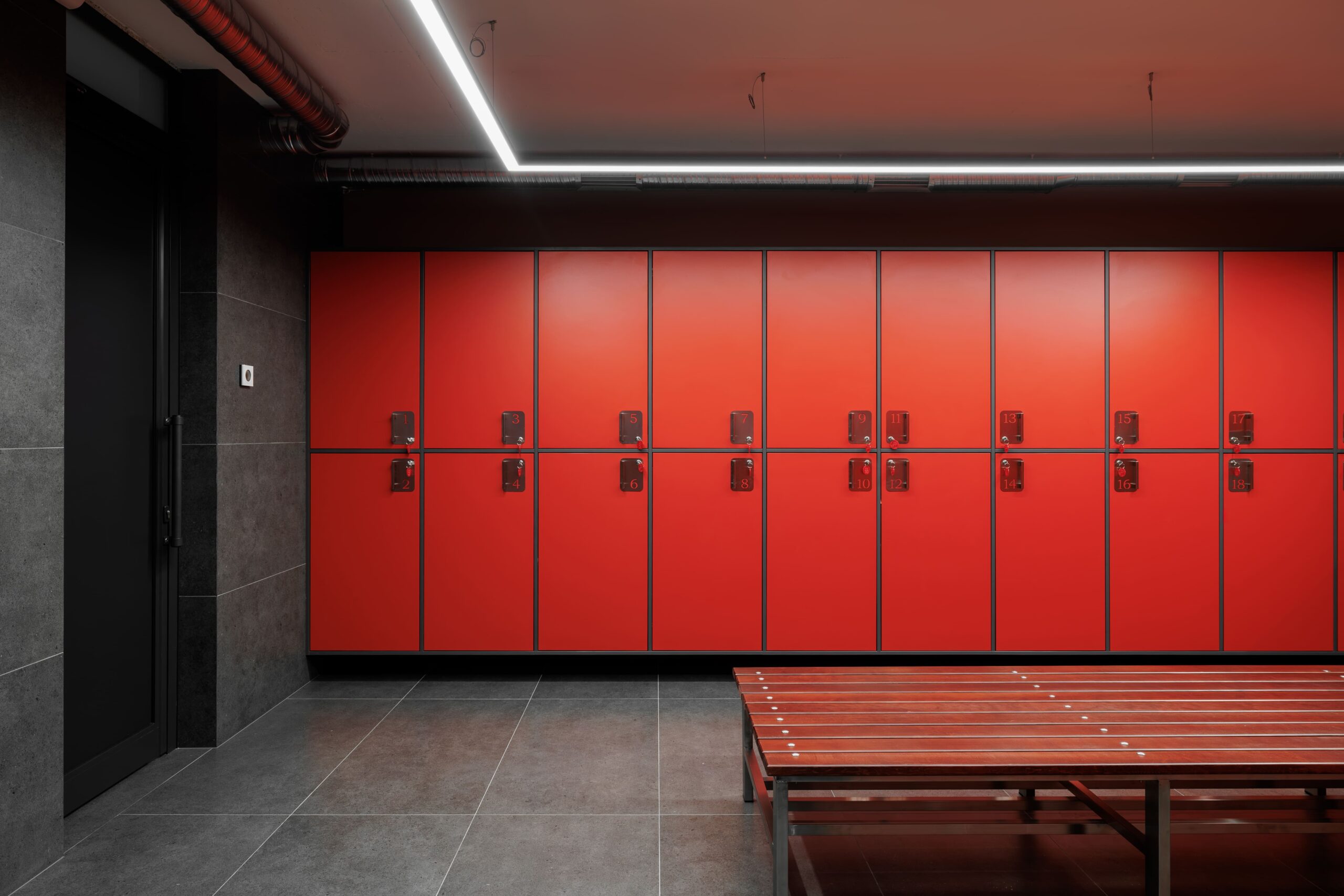 Full wall of numbered red lockers with timber bench