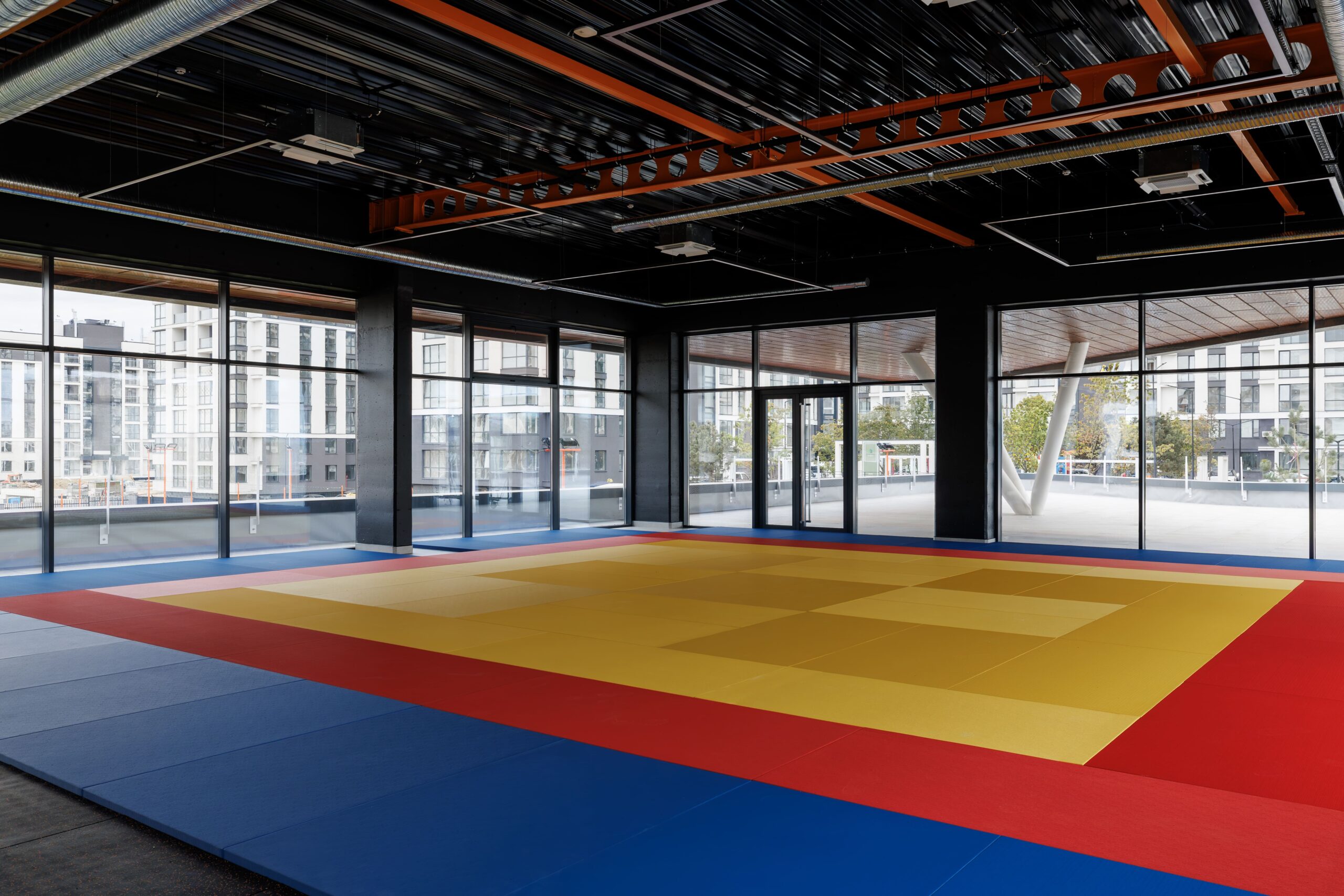 Training hall with colorful tatami mats and exposed black ceiling with timber baffles