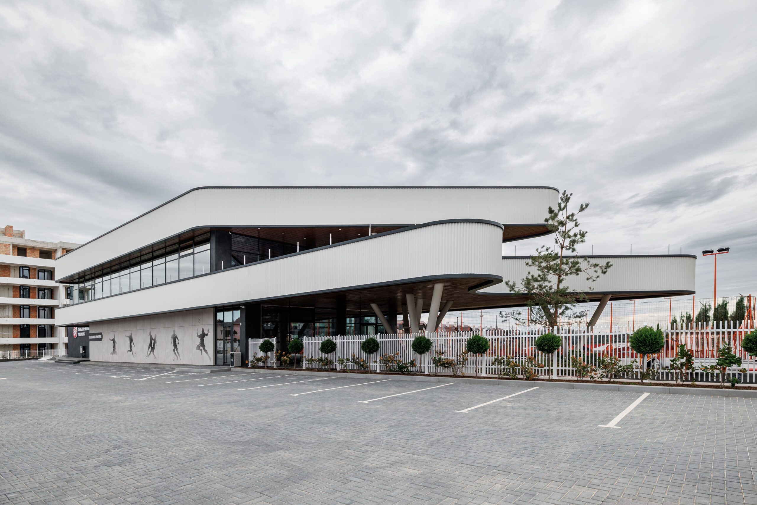 Curved white facade of Premier Football Club Training Center with athlete silhouettes on wall