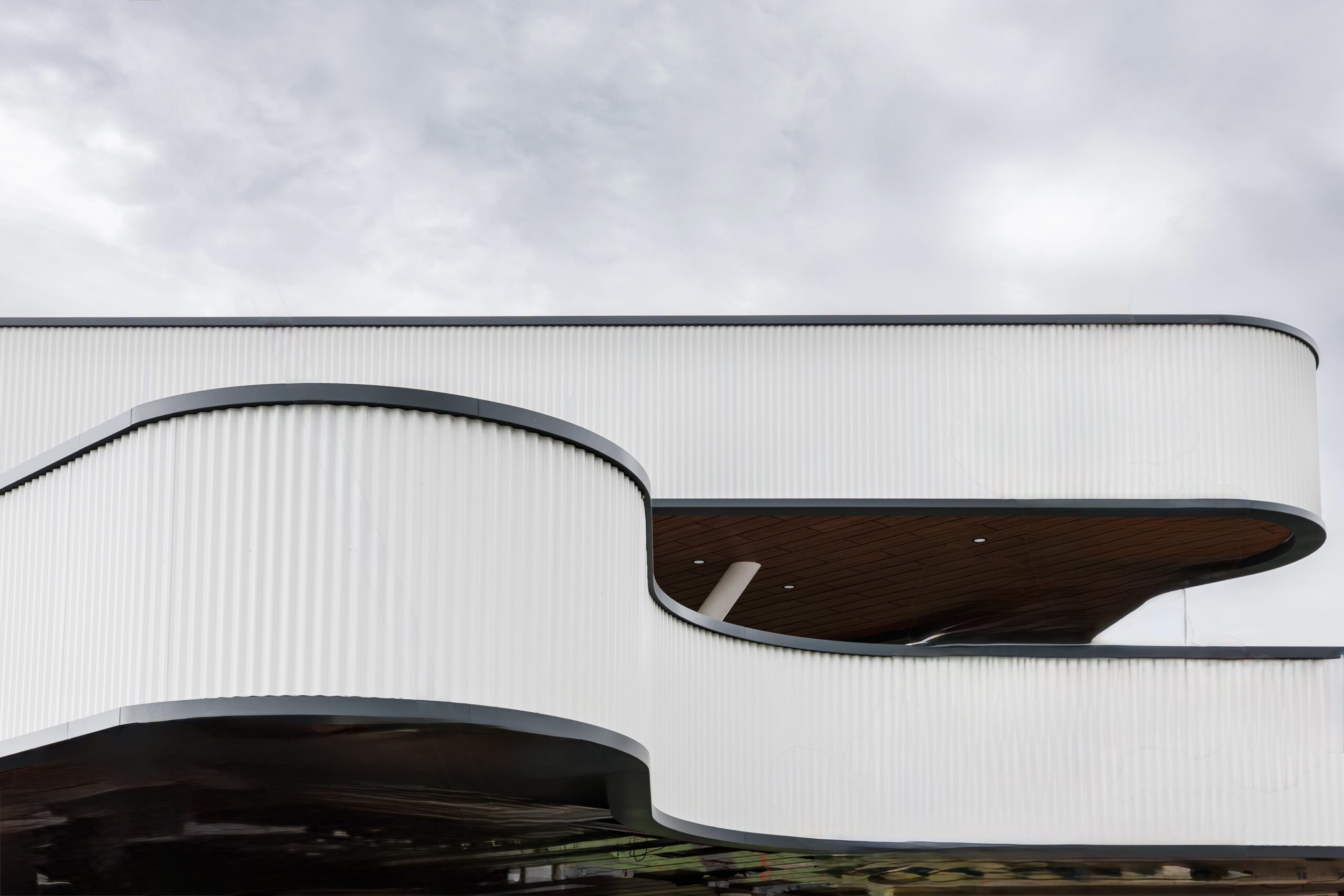 Close-up of curved white corrugated facade with floating balcony overhang