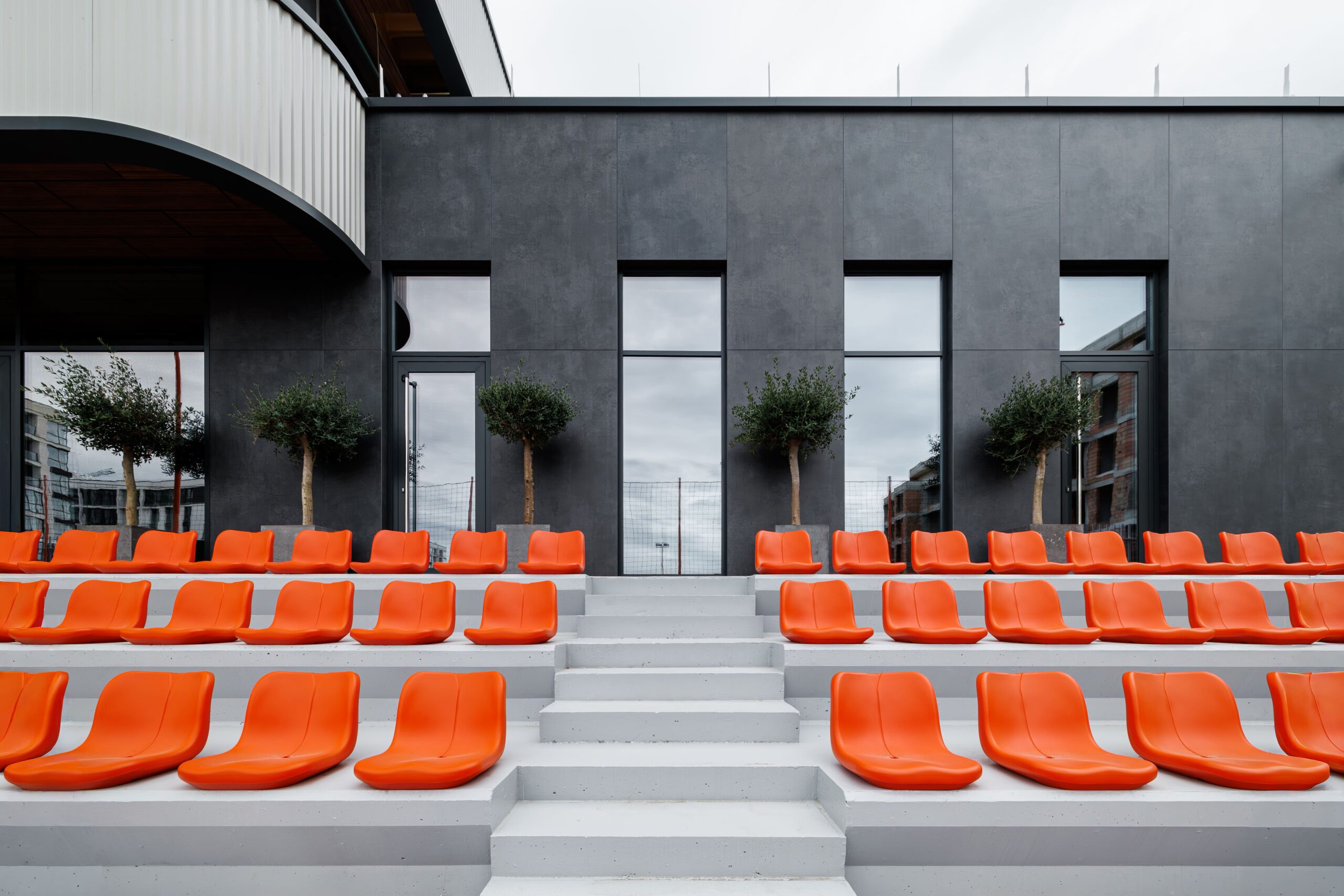 Orange stadium seats against dark gray facade with olive trees