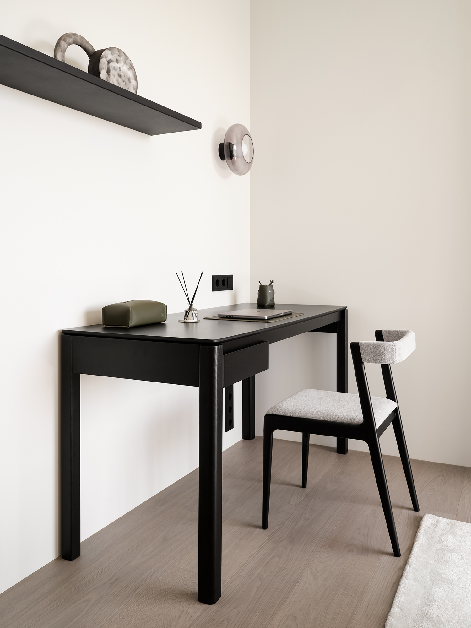 Black minimalist desk with floating shelf and round wall sconce