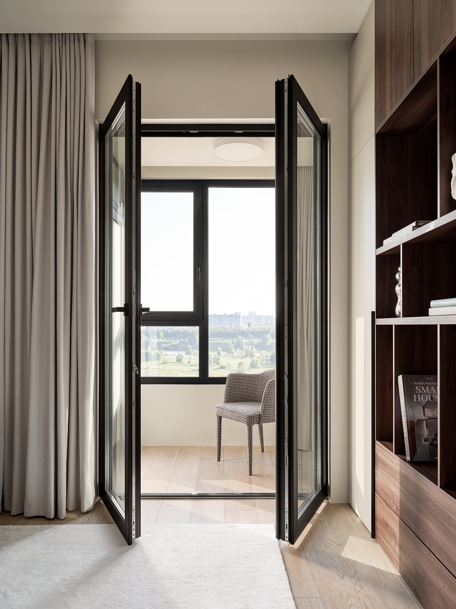 View through black-framed folding glass doors to loggia with chair and city view